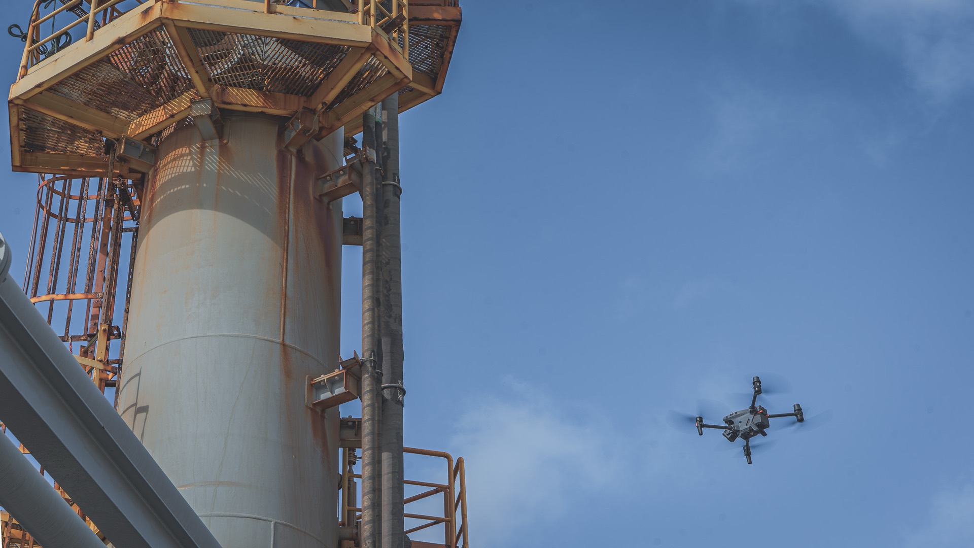 Inspection drone flying alongside an industrial stack during a non-destructive testing survey
