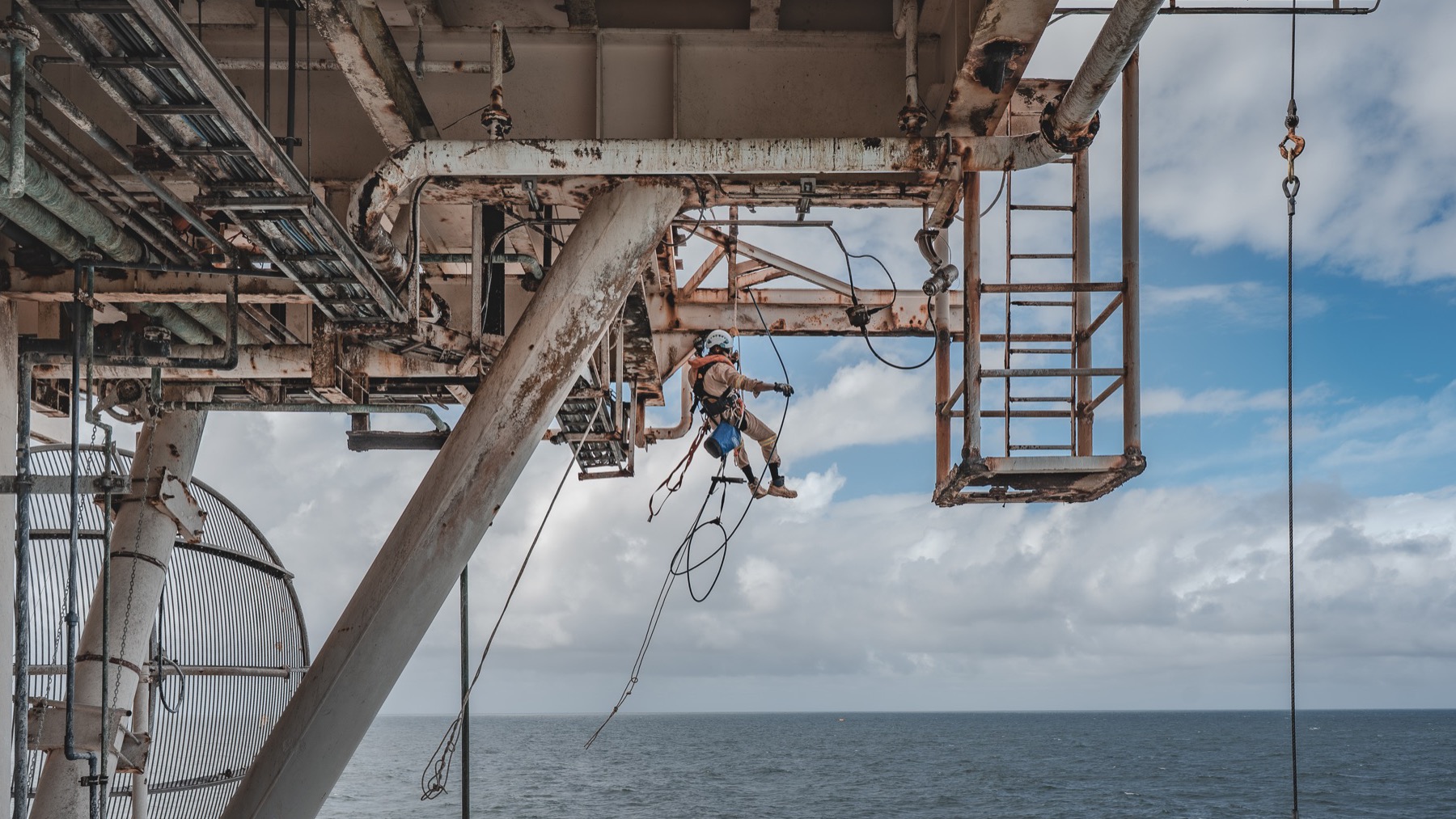 Rope-access technician descending beneath an offshore platform over the sea